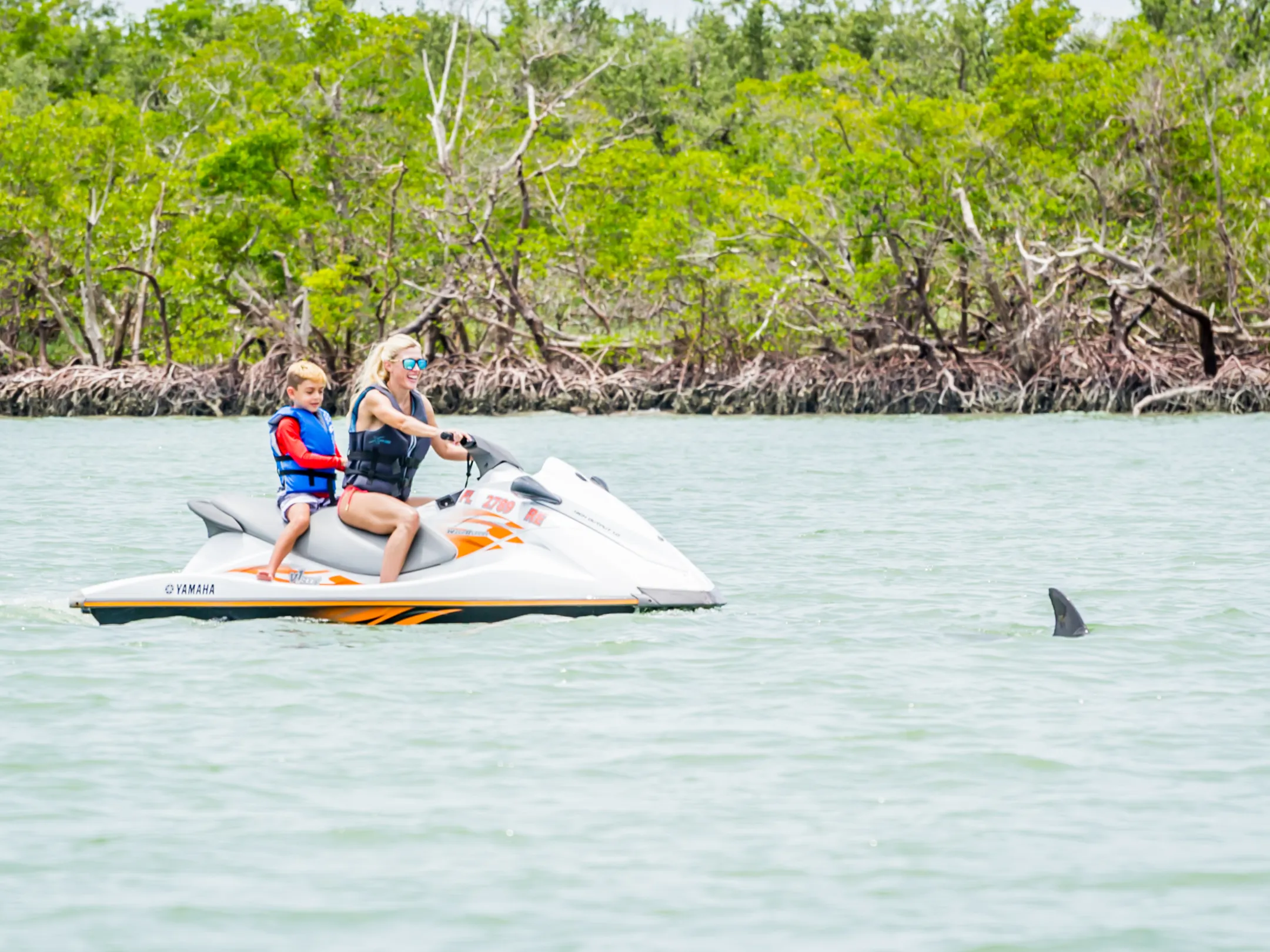 a woman and child riding on a jet ski with a dolphin in the water